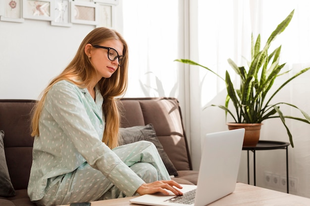 Side view of woman in pajamas working on laptop at home