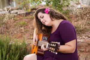 Free photo side view of woman playing guitar with flower in hair