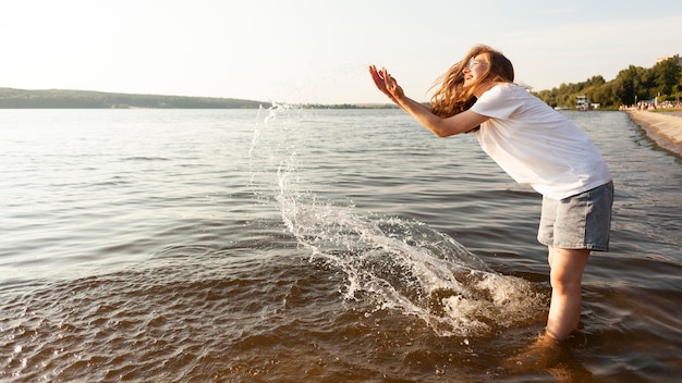 Free photo side view of woman playing with water by the lake