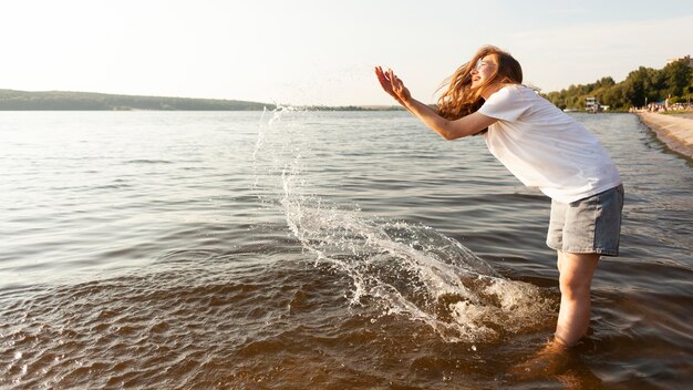Вид сбоку женщины, играющей с водой на берегу озера