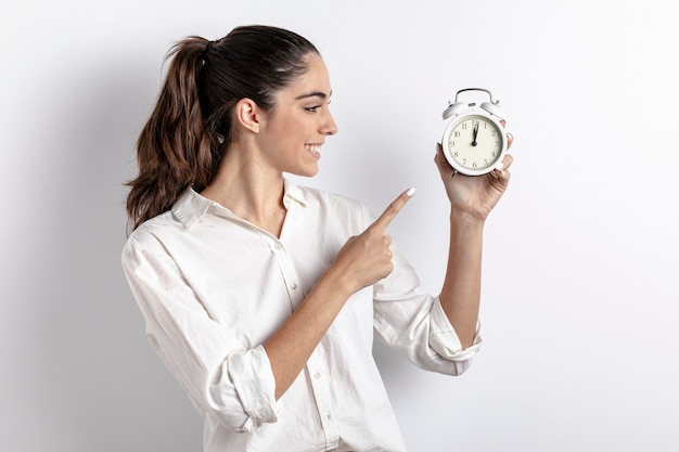 Side view of woman pointing at hand held clock