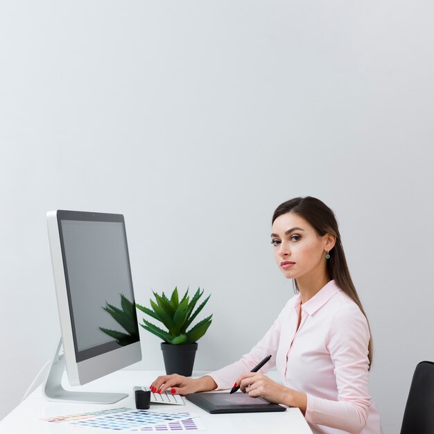 Side view of woman posing at desk while using tablet