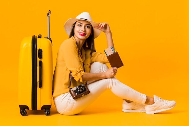 Side view of woman posing next to luggage while holding travel essentials