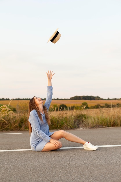 Free photo side view of woman posing in the middle of the road with hat