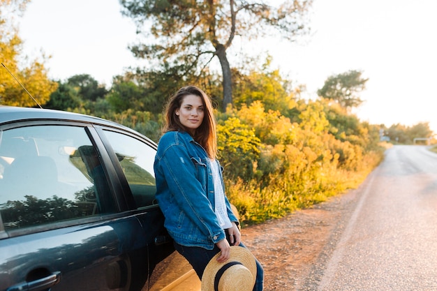 Side view of woman posing outdoors next to car