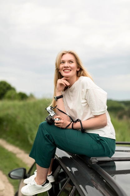 Side view of woman posing on top of car while holding camera