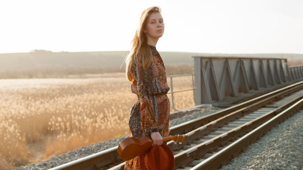 Foto gratuita vista laterale della donna che posa sulle piste del treno mentre tenendo ukulele