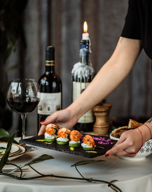 Side view of a woman putting a board with fried shrimps on grilled avocado topped with cream sauce