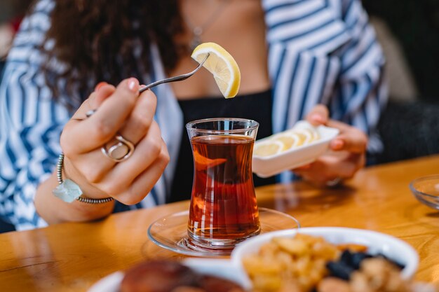 Side view of a woman putting a lemon slice into armudu glass with black tea