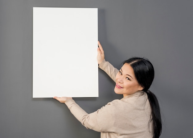 Side view woman putting on wall balnk paper sheet