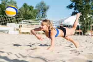 Free photo side view of woman reaching to hit volleyball before it hits the sand