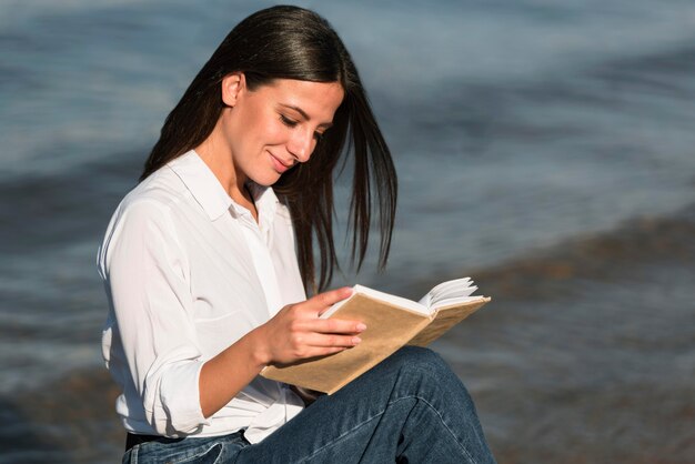 Женщина, читающая книгу на пляже, вид сбоку