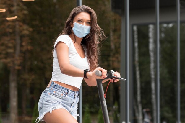Side view of woman riding electric scooter while wearing medical mask