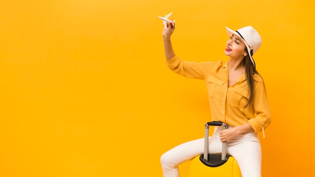 Side view of woman sitting on luggage and holding plane figurine with copy space