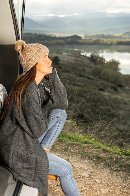 Free photo side view of woman sitting on the  trunk of the car while on a road trip