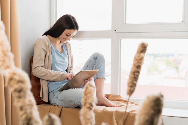 Side view of woman sitting next to window and working on tablet