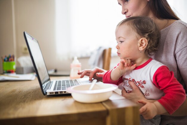 Free photo side view of a woman sitting with her child using laptop over wooden desk