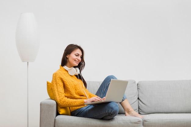 Side view of woman smiling while sitting on sofa and looking at laptop