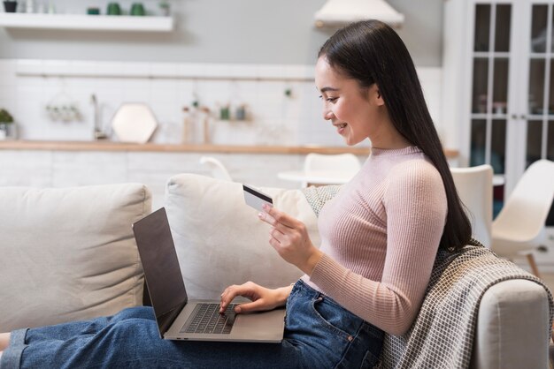 Вид сбоку женщины на диване, делая покупки онлайн