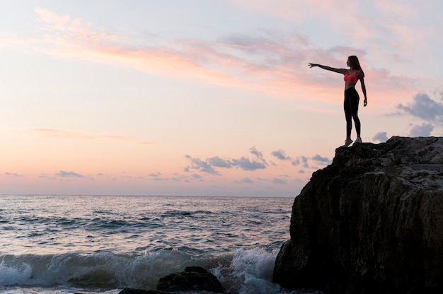 Side view woman in sportswear standing on a coast with copy space