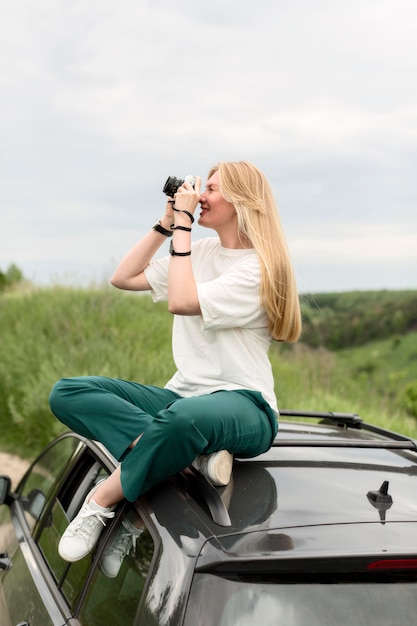 Side view of woman standing on car and taking nature pictures