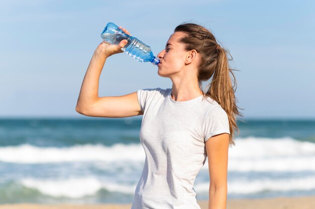 Side view of woman staying hydrated during beach workout