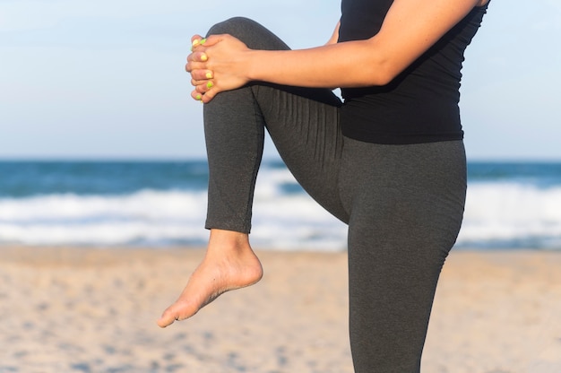 Вид сбоку на женщину, растягивающую ноги на пляже перед тренировкой