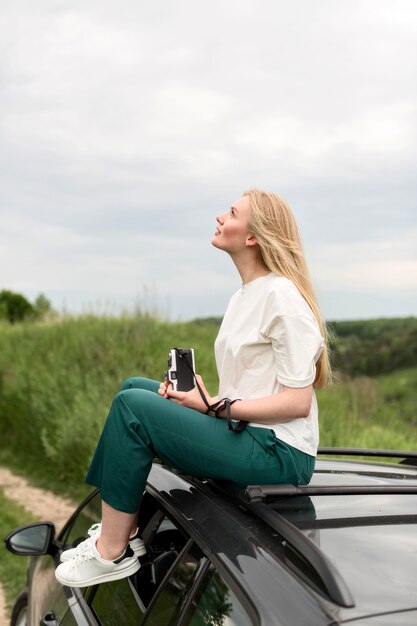 Side view of woman on top of car holding camera