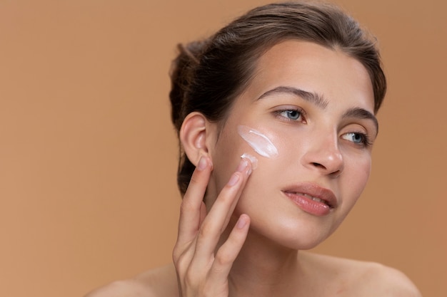 Free photo side view woman using face cream