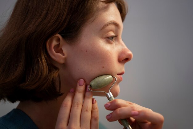 Side view woman using face roller for massage