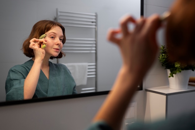 Free photo side view woman using face roller for massage