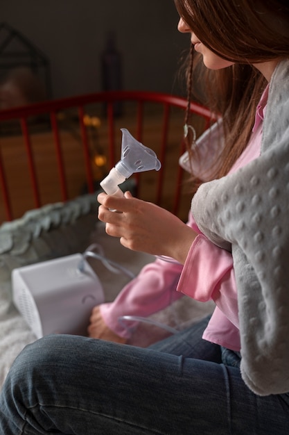 Free photo side view woman using nebulizer at home