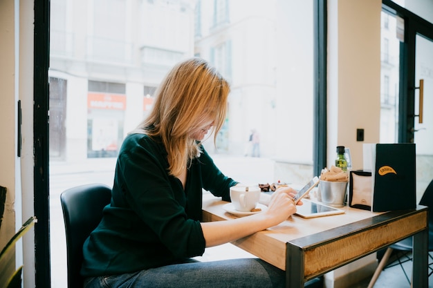 Вид сбоку женщина с помощью смартфона в хорошем кафе