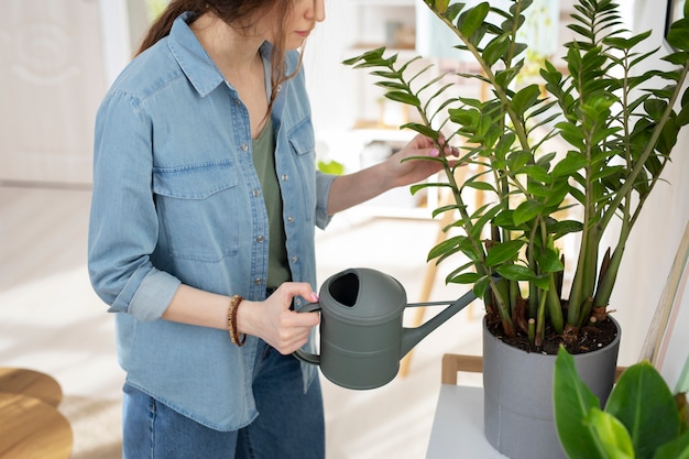 Вид сбоку женщина поливает растение дома