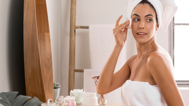 Side view woman wearing towels and using cream