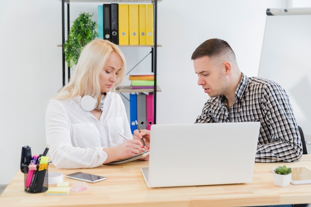 Side view of woman in wheelchair and colleague conversing at desk