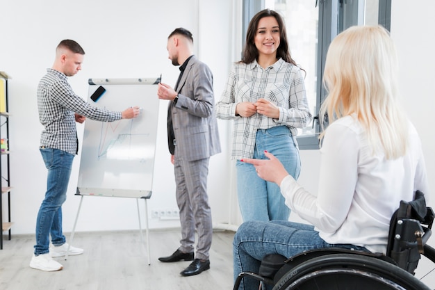 Free photo side view of woman in wheelchair conversing with coworker at the office