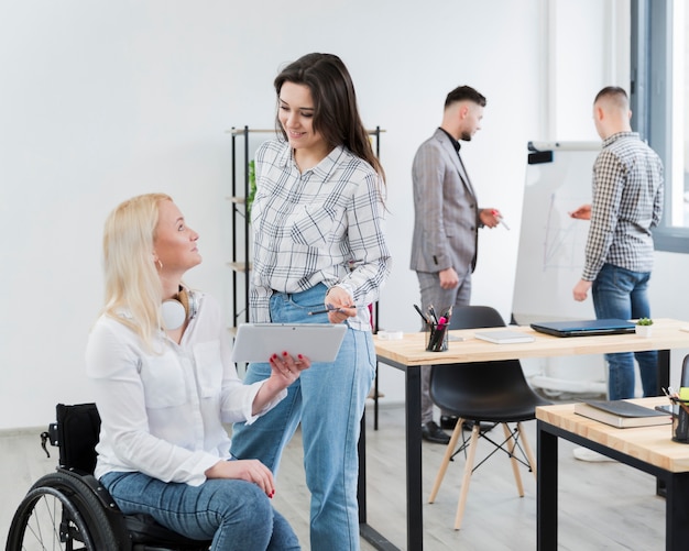 Side view of woman in wheelchair conversing with female colleague at office