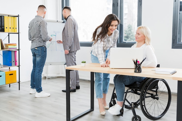Free Photo side view of woman in wheelchair conversing with female coworker at the office
