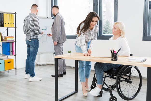Side view of woman in wheelchair conversing with female coworker at the office