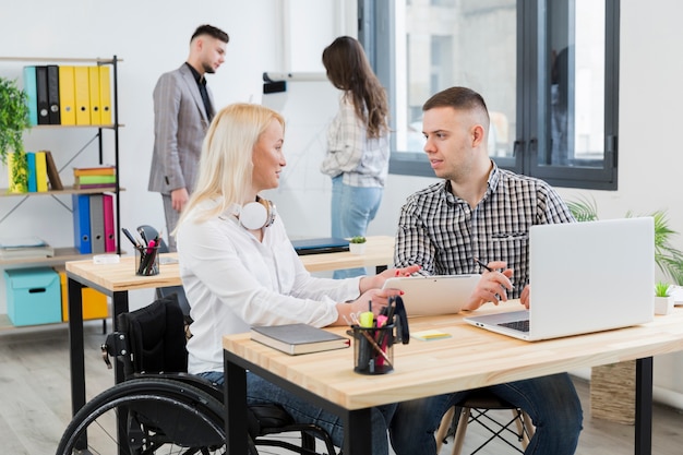 Free photo side view of woman in wheelchair discussing with coworker at her desk