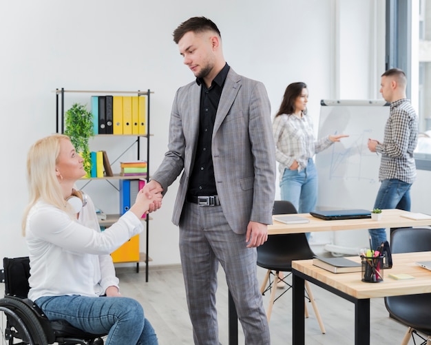 Side view of woman in wheelchair shaking hands with colleague