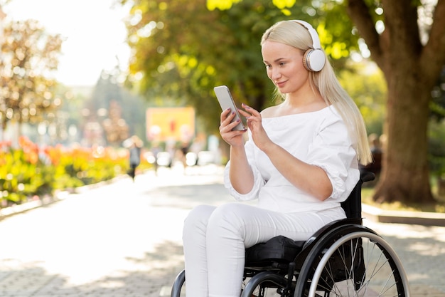 Вид сбоку женщины в инвалидной коляске со смартфоном и наушниками