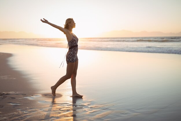 腕を伸ばしてビーチに立っている女性の側面図