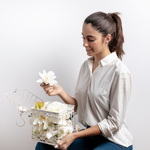 Vista laterale della donna con gabbia per uccelli e fiori