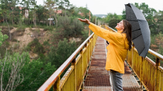 Free photo side view woman with black umbrella rising her hand