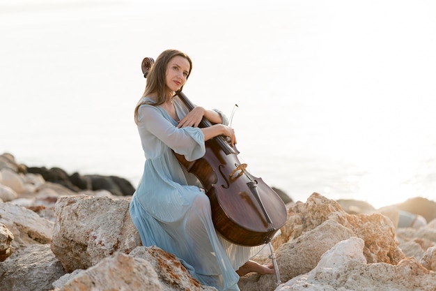 Вид сбоку женщины с виолончелью на скалах