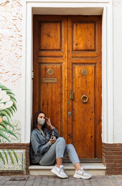 Side view of woman with face mask and camera next to door outside