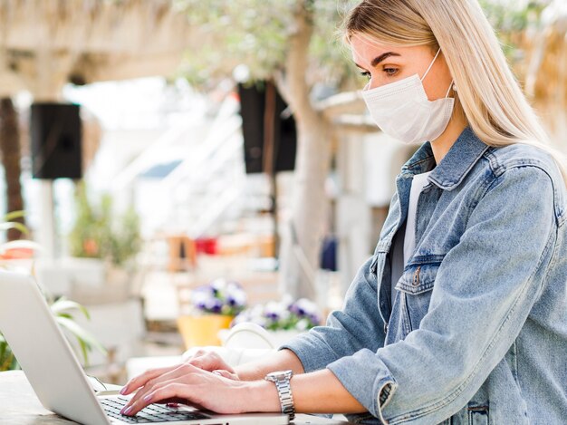 Вид сбоку женщины с маской, работающей на ноутбуке