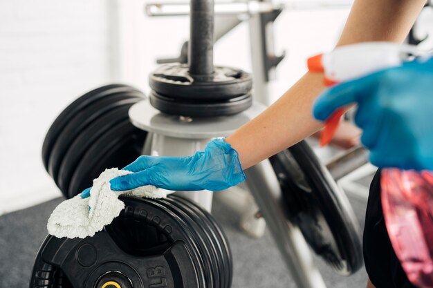 Side view of woman with gloves at the gym disinfecting equipment